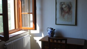 A room with a wooden table, a chair, a radiator, a window with an open shutter, and a framed artwork on the wall. - La Locanda del Barbagianni (Santa Luce)