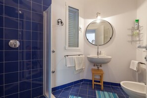 Un baño con piso de azulejos azules, un lavamanos blanco, un espejo y un taburete de madera.
