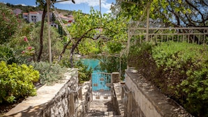 A stone pathway leading to a pool area surrounded by lush greenery and a metal fence. - Holiday home Duje (Okrug)