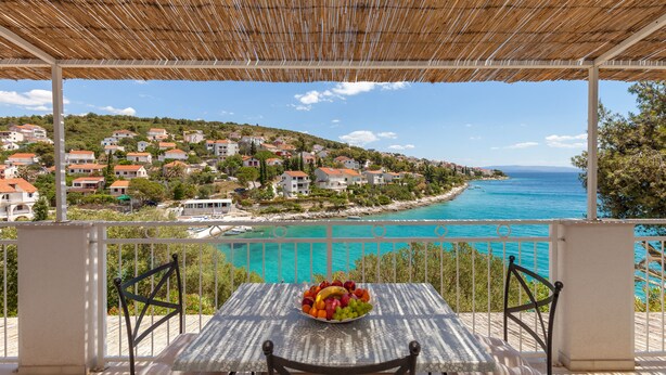 A table with a fruit bowl, a white tablecloth, and a view of a coastal town and sea. - Holiday home Duje (Okrug)