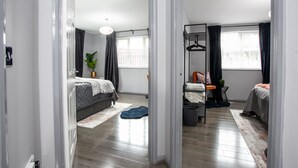 A modern bedroom with a large bed, a bedside table, a dresser, and a window with curtains. - Trafford Place (Manchester)