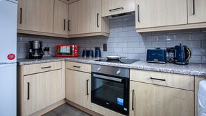 A kitchen with light wooden cabinets, a stainless steel oven, a microwave, a coffee maker, and a toaster. - Trafford Place (Manchester)