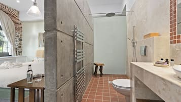 Un baño moderno con ducha, inodoro y lavamanos. Hay un taburete de madera y una botella de agua sobre una mesita.