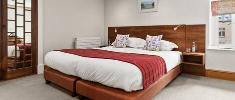 A bedroom with a large bed, wooden headboard, a nightstand, a radiator, and a window with a view of buildings.