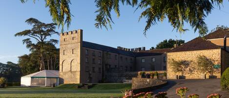 A historic stone building with a tower, a covered pavilion, and a well-maintained lawn.