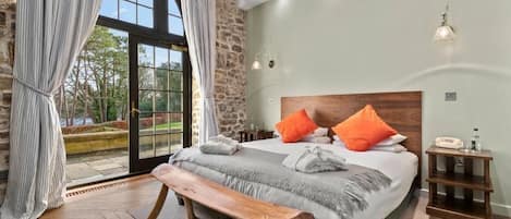 A bedroom with a large bed, a bench, a nightstand, and a view of the outdoors through a glass door.