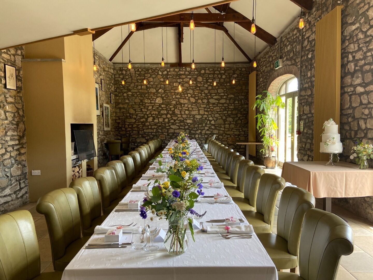 A long dining table with leather chairs, set for a formal meal, in a room with stone walls and wooden beams.