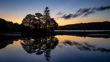 Escena serena junto al lago, con aguas tranquilas que reflejan árboles y un cielo al atardecer.