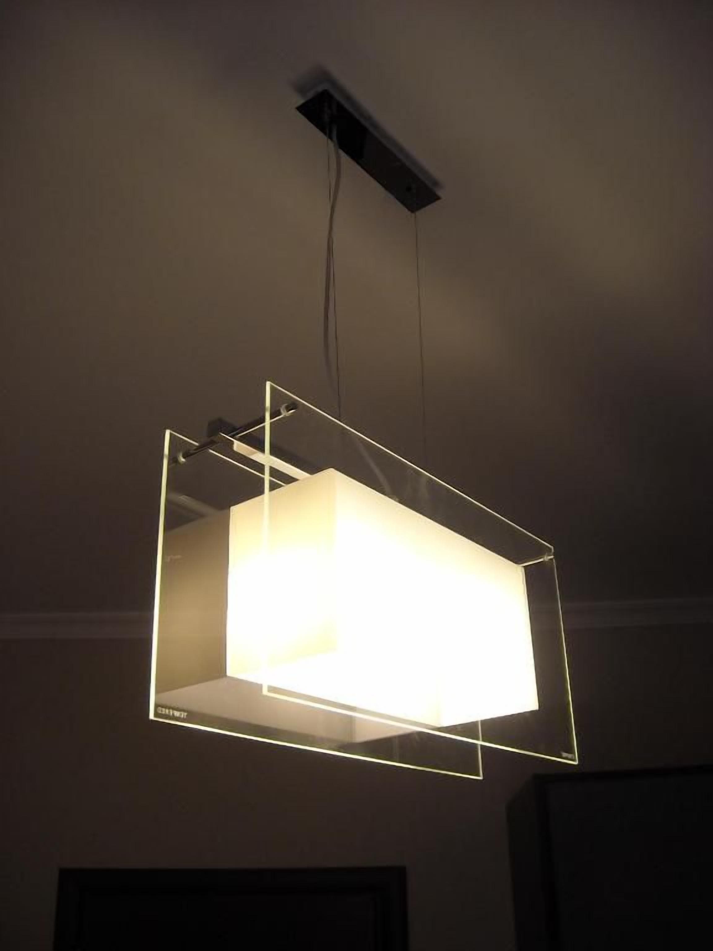 A rectangular light fixture with a white frame and a glowing interior, hanging from a ceiling with a visible electrical cord.
