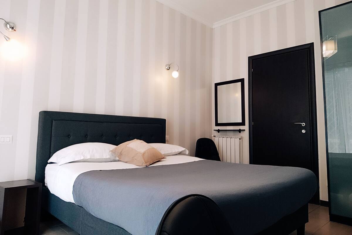 A neatly arranged bedroom with a bed, a bedside table, a chair, a radiator, and a door.