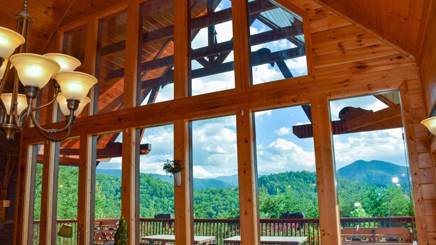 A wooden interior with large windows, a chandelier, and a view of a forested mountain range.