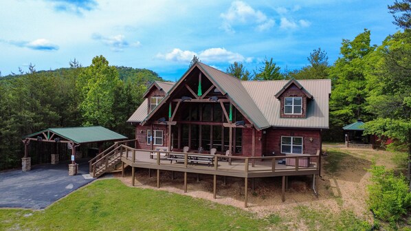A lodge with a covered deck, a staircase, and a view of the surrounding forest. - Brookstone Lodge - 6 Bedroom -Dog Friendly-Pool Access-Theater-Game Room-Hot Tub (Sevierville)