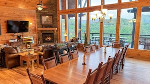 A cozy cabin interior with a fireplace, wooden furniture, a large dining table, and a TV.