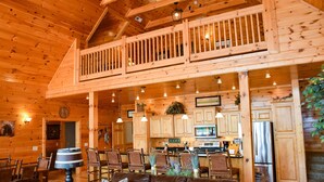 A wooden cabin interior with a dining area, kitchen, and a balcony.