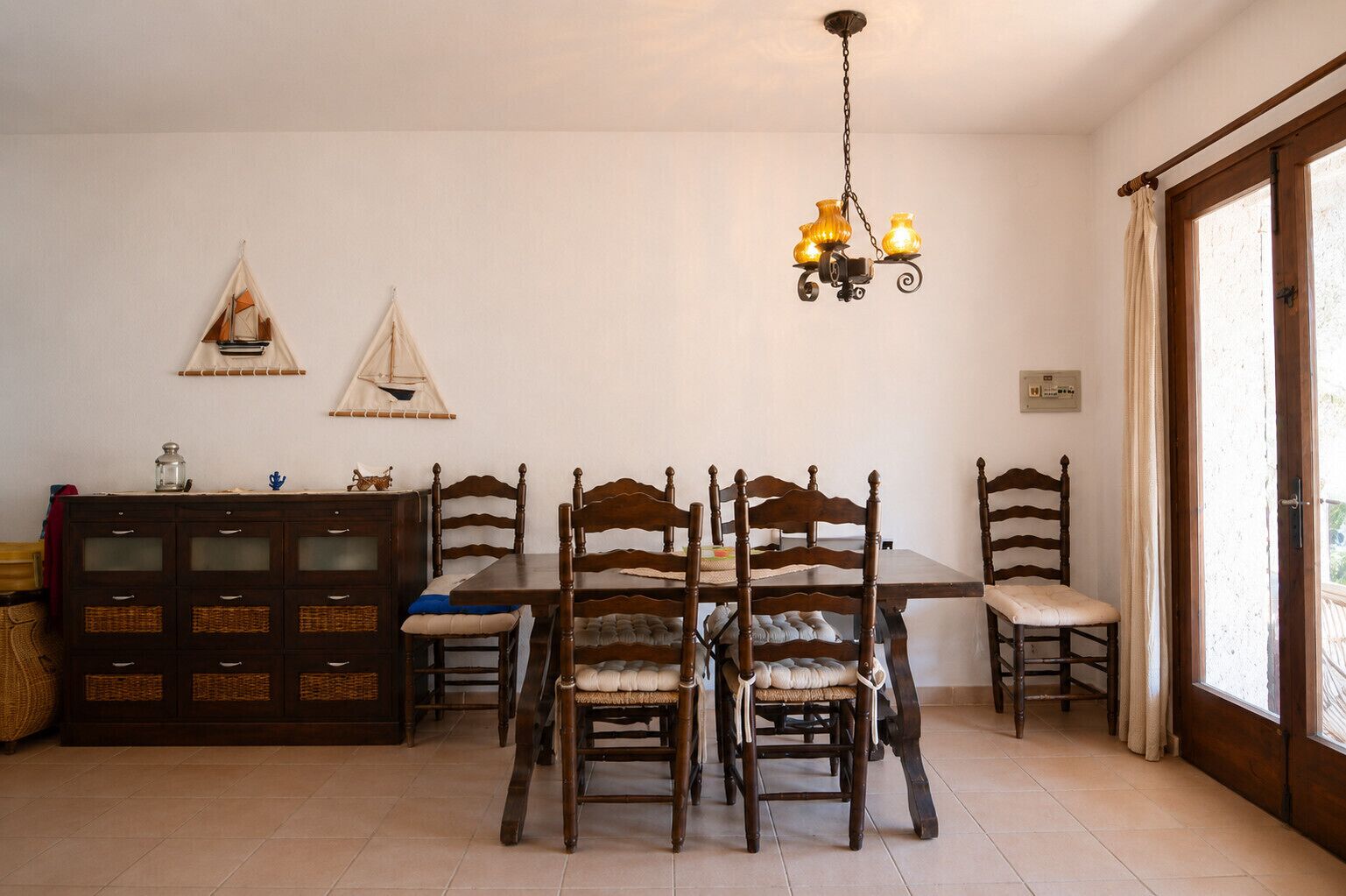 Un coin repas avec une table et des chaises en bois, un lustre et un meuble avec des tiroirs.