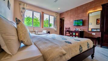 A bedroom with a large bed, a television on the wall, and a window with curtains.