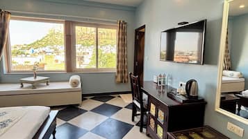 Quarto de hotel com cama, escrivaninha, cadeira, televisão, espelho, janela com vista para uma colina e chão quadriculado.