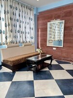 A room with a sofa, a glass-top coffee table, a vase with flowers, a mirror, and a patterned floor.
