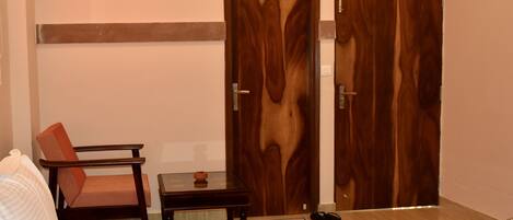 A hotel room with a bed, a chair, a small table, a TV mounted on the wall, and two wooden doors.