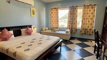 A bedroom with a bed, a bedside table, a chair, a window with curtains, a ceiling fan, and a checkered floor.