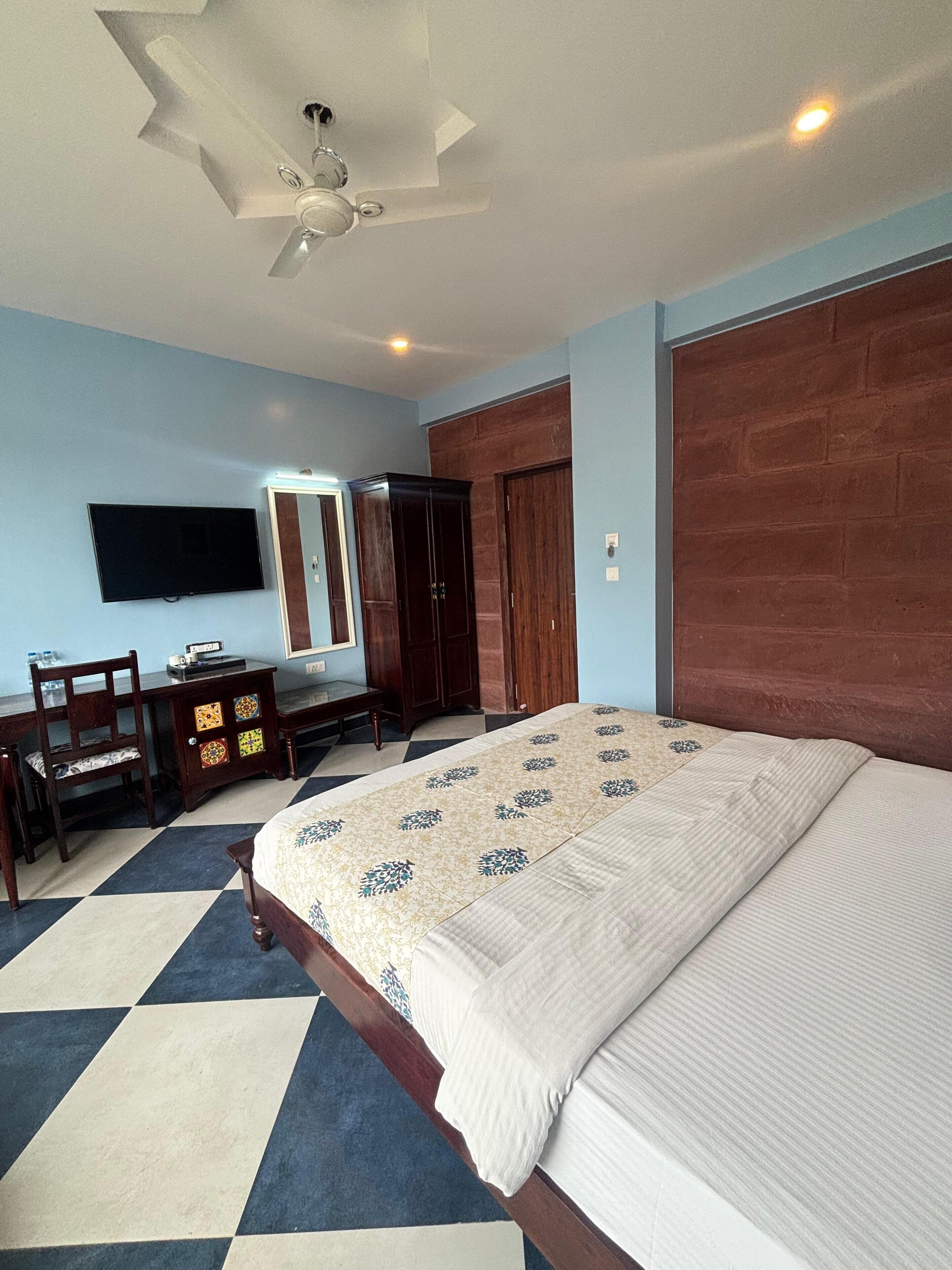 A bedroom with a bed, a desk, a chair, a television, a wardrobe, and a ceiling fan.