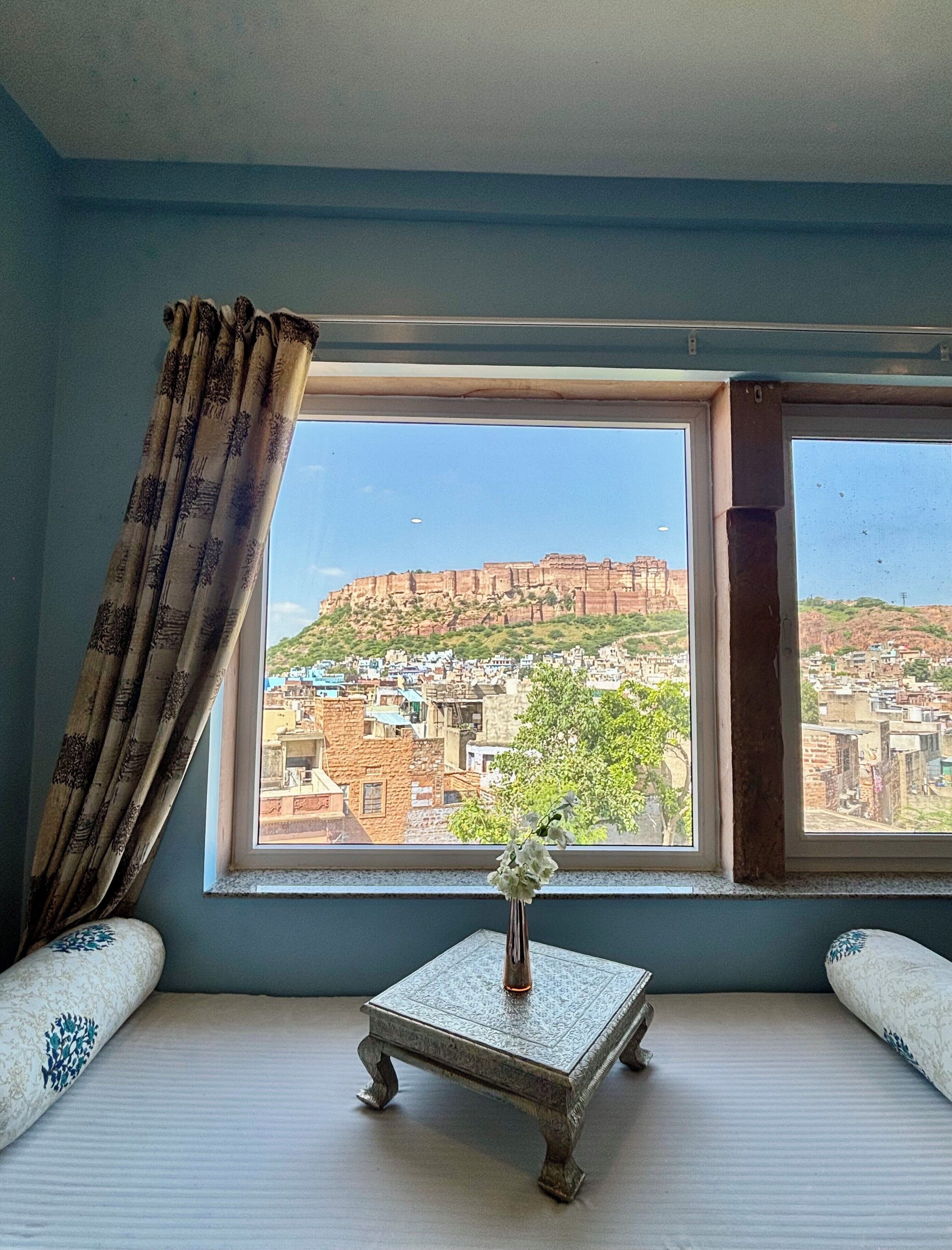 Una habitación con un ventanal grande, una mesita con un florero y cortinas estampadas.