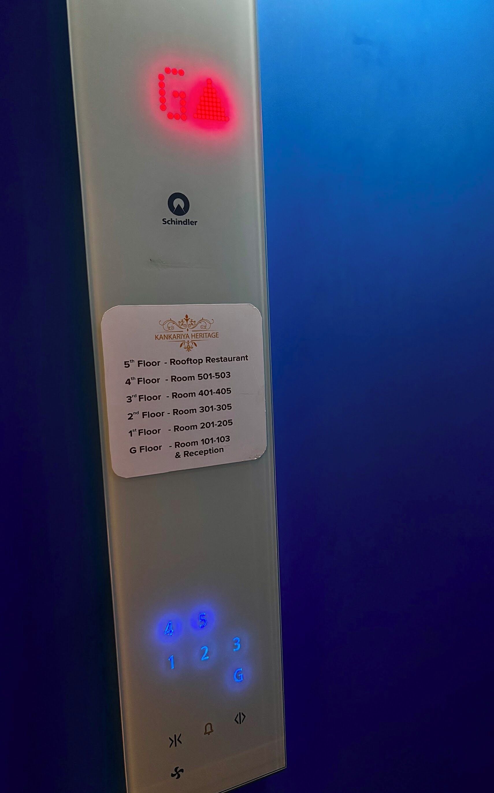 Bedieningspaneel van een hotel lift met een digitaal scherm, een Schindler logo en een bordje met kamerindelingen per verdieping.
