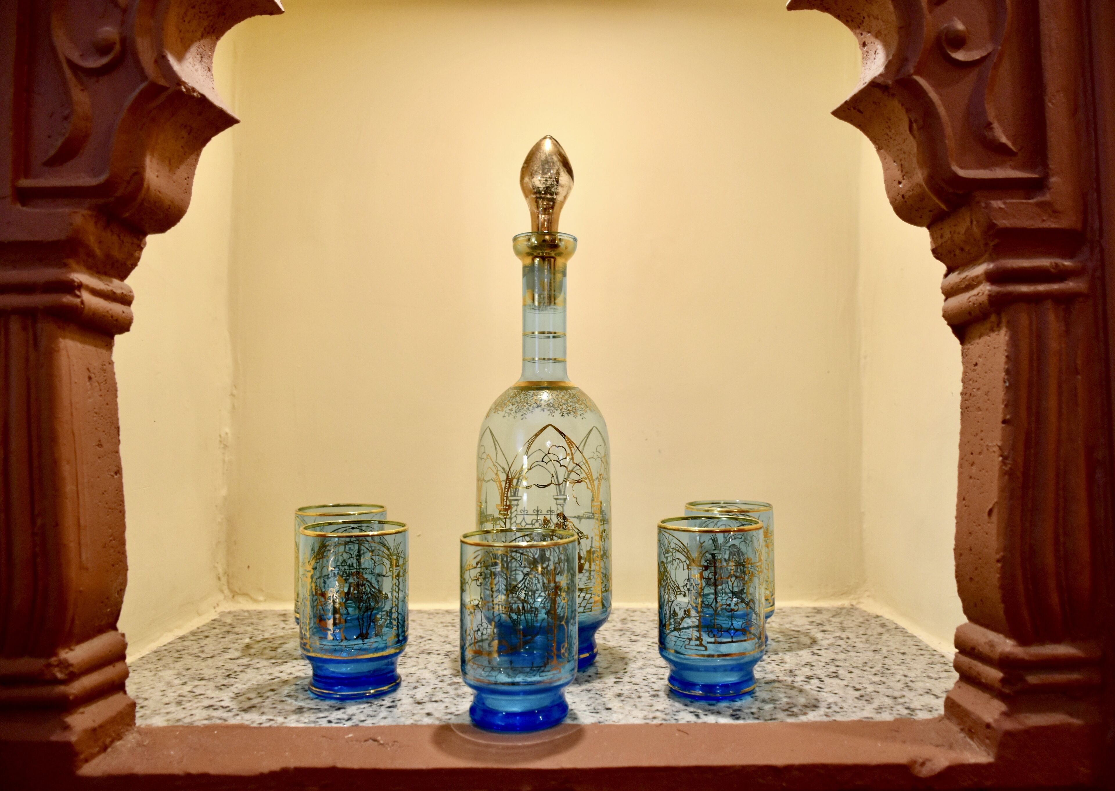 A bottle and four glasses on a shelf.