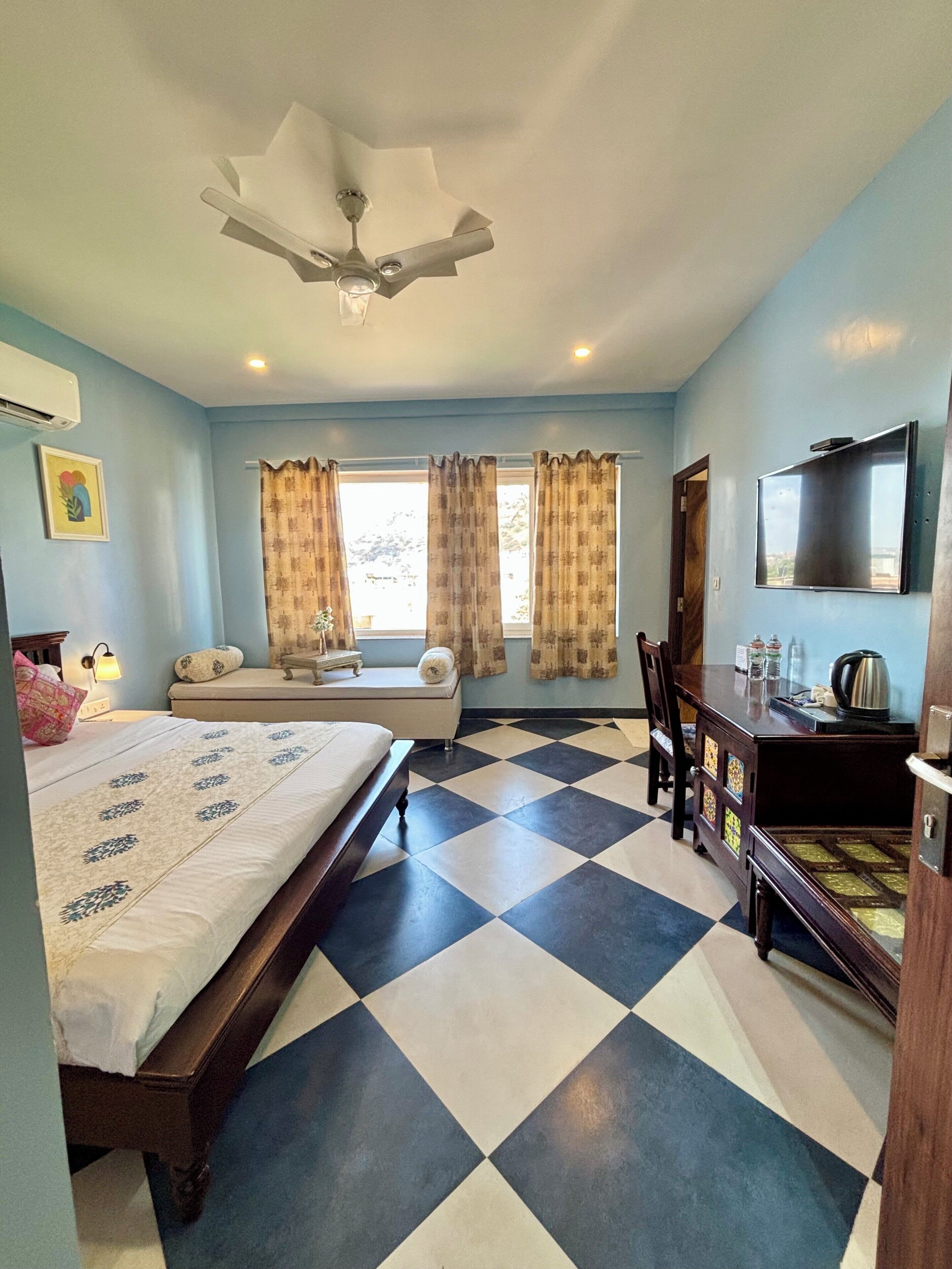 A hotel room with a bed, a desk, a chair, a television, and a ceiling fan.