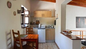A compact kitchen with wooden cabinets, a small refrigerator, and a dining area with a wooden table and chairs. - Palmera, quiet studio with terrace and view to the mountains (Las Zocas)