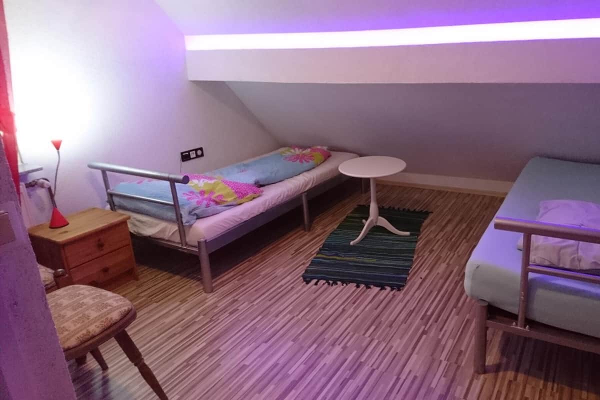 Une chambre de taille modeste, équipée de deux lits simples, d’une petite table, d’une chaise et d’une lampe de chevet.