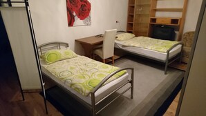 Une petite pièce, de taille modeste, comprenant deux lits simples, un bureau et une chaise.