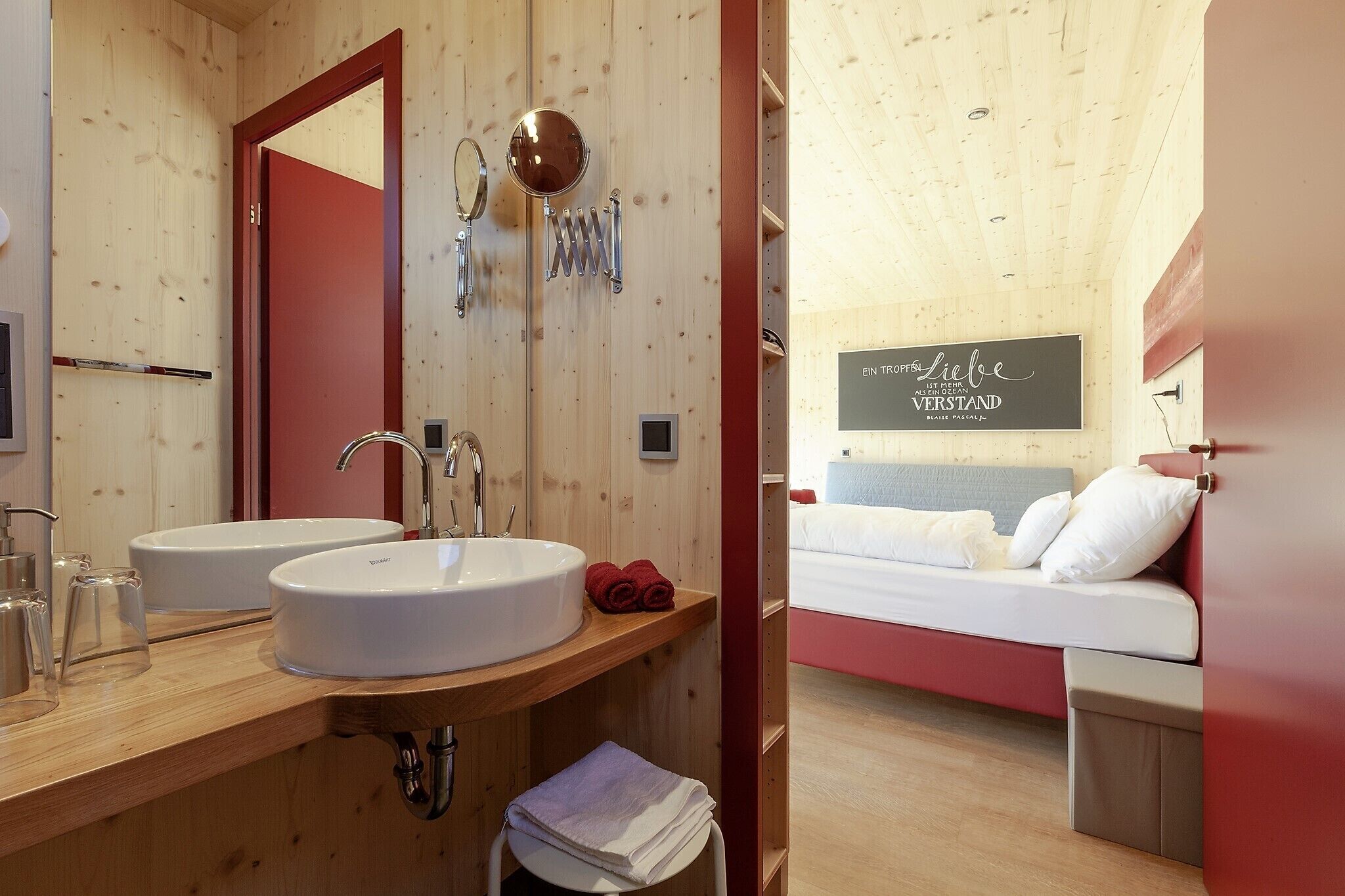 A wooden interior with two sinks, a mirror, and a bed with a red wall and a sign.