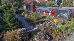 Un edificio moderno con techo de vidrio, rodeado de un jardín con diversas plantas y un camino de piedra.