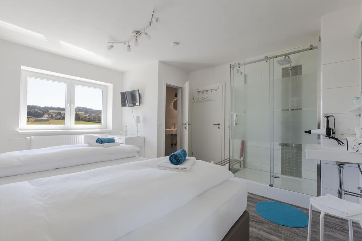 Quarto de hotel moderno com duas camas, chuveiro e banheiro com box de vidro.