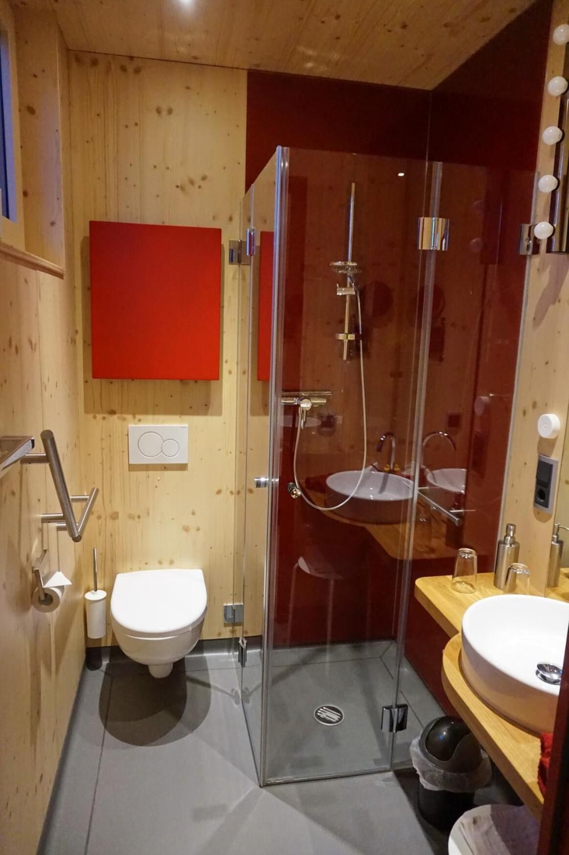 A modern bathroom with a glass-enclosed shower, a wooden vanity, and a toilet.