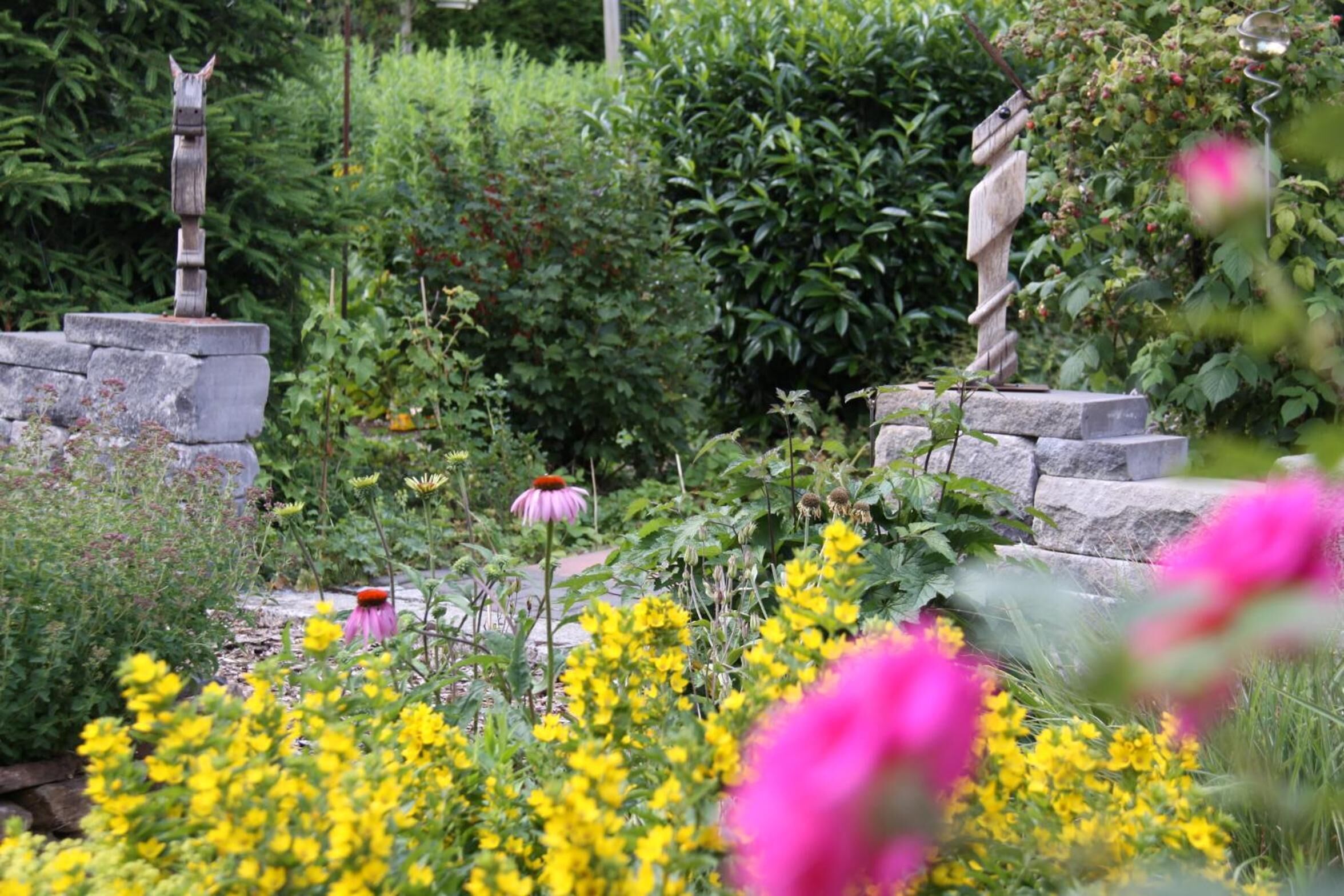 Um jardim com uma escultura de pedra, diversas plantas e flores.