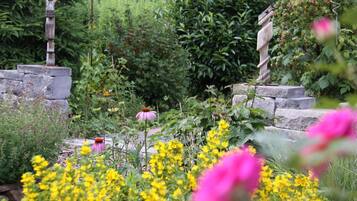 Um jardim com uma escultura de pedra, diversas plantas e flores.