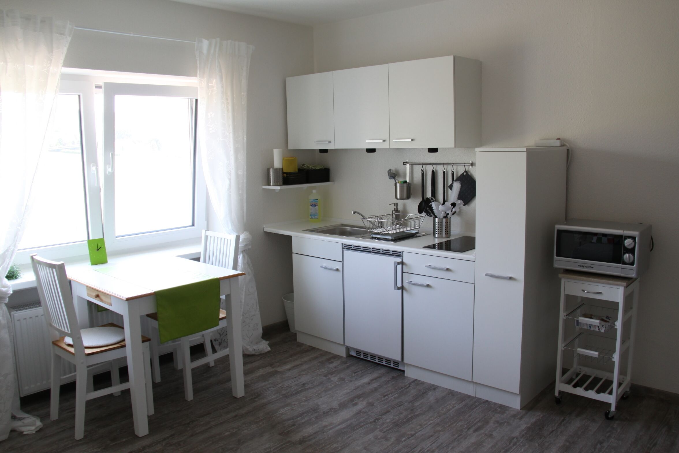 A compact kitchen with white cabinetry, a microwave, and a small refrigerator.