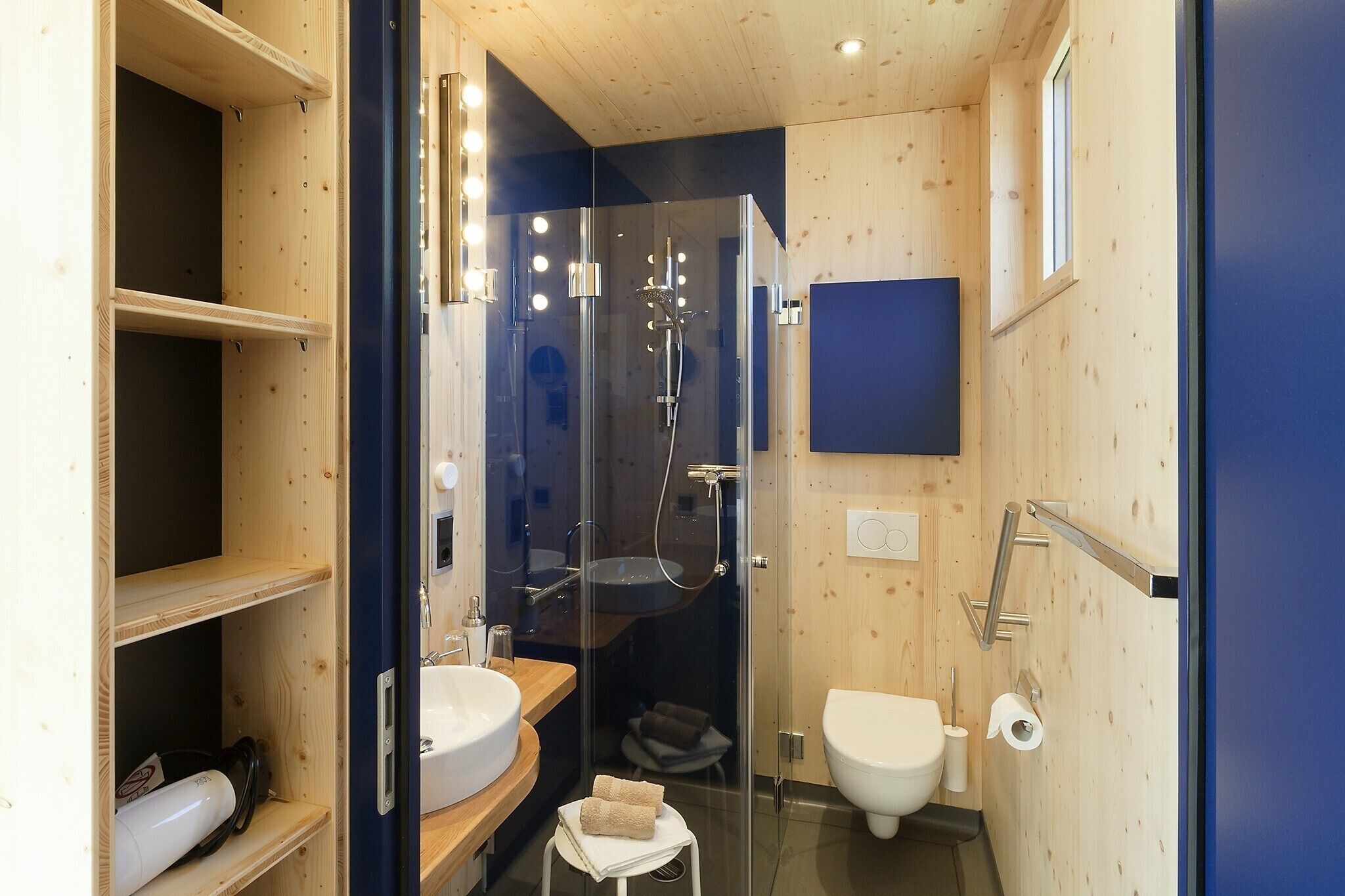 Un baño moderno y compacto con ducha envuelta en vidrio, un lavabo e inodoro.