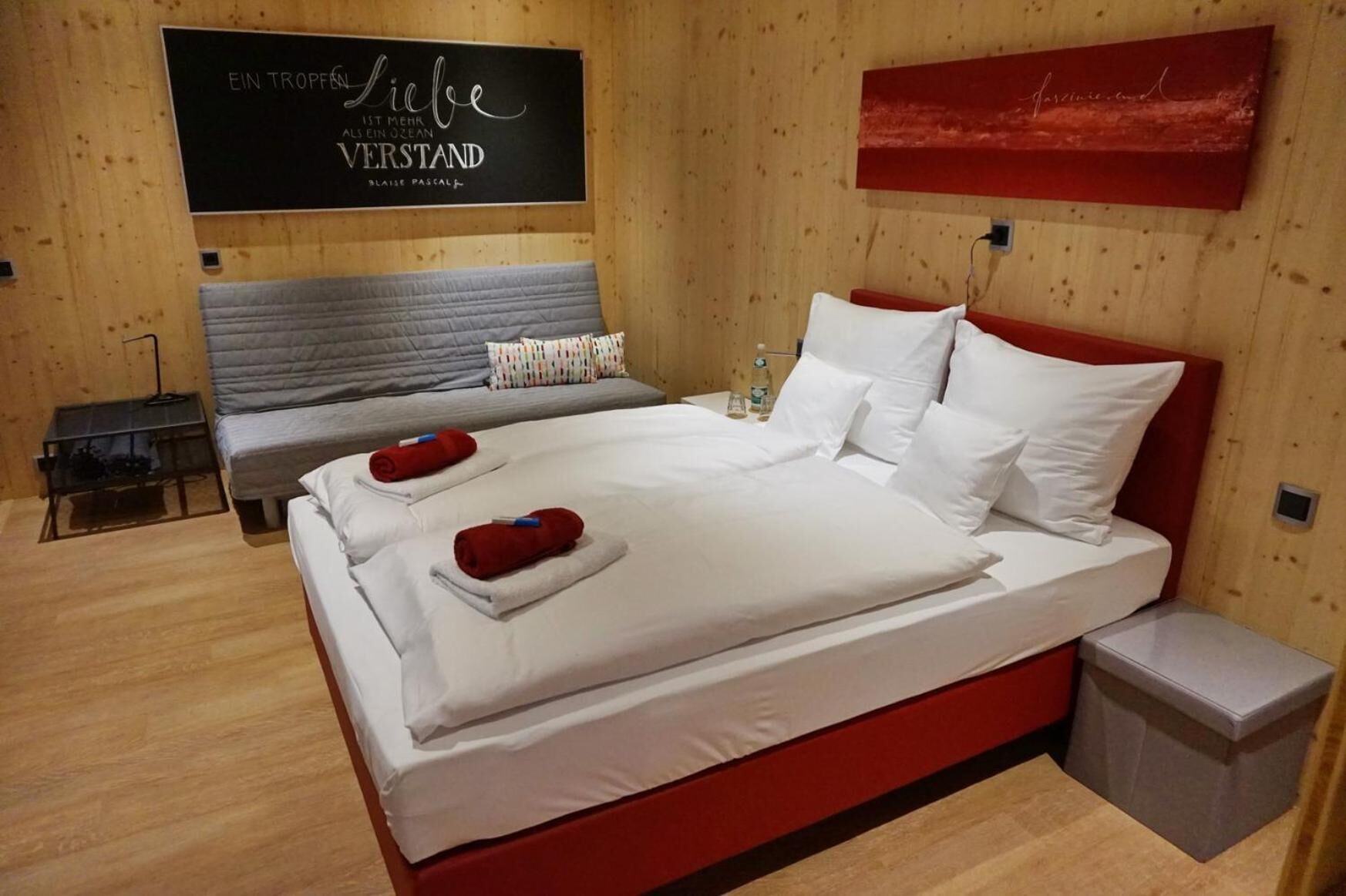 Ein modernes Hotelzimmer mit einem großen Bett, zwei Nachttischen, einem Beistelltisch und einer Holzwand mit einem Schild.