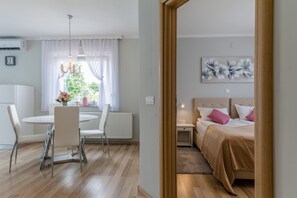 A modern room with a round dining table, white chairs, a bed with pink and white bedding, and a window with sheer curtains. - Apartments Snježana Rastoke (Slunj)