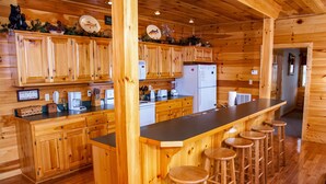 Cuina d'una cabana de fusta amb armaris de fusta, una illa central amb tamborets i un refrigerador.