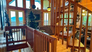 A spacious cabin interior with a stone fireplace, a Christmas tree, and a wooden staircase. - Paradise Found - Cabin (Sevierville)