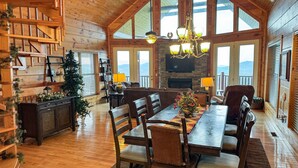 A spacious log cabin interior with a dining area, fireplace, and large windows offering mountain views. - Paradise Found - Cabin (Sevierville)