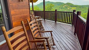 Un pontile in legno con sedie, un muro di legno e vista sulle colline verdi.