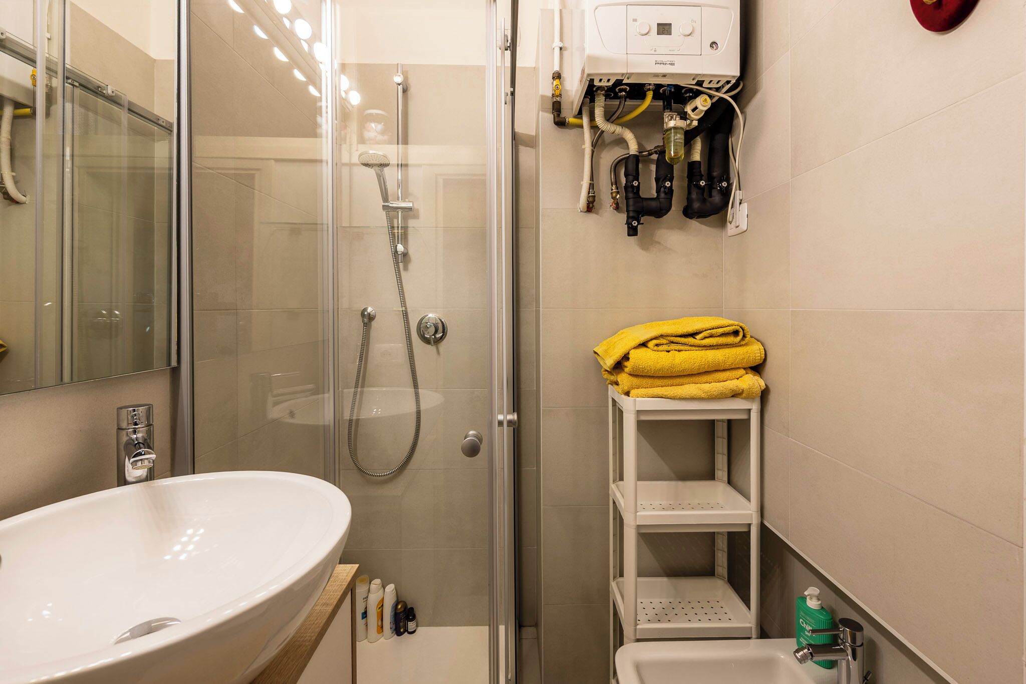 Une salle de bain avec une douche à parois de verre, un lavabo blanc et une étagère avec des serviettes jaunes.
