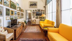 Una sala de estar con un sofá amarillo, muebles de mimbre, un televisor y una pared decorada con cuadros.
