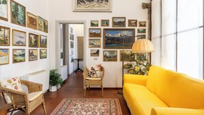 Una sala de estar con un sofá amarillo, sillas de mimbre, un tapete estampado y una pared decorada con cuadros de paisajes.