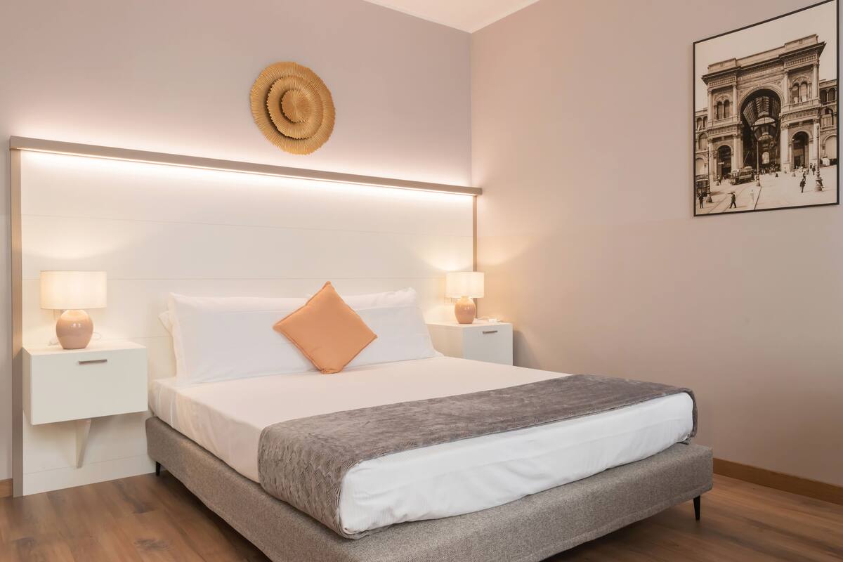 A modern bedroom with a large bed, two bedside tables, and a wall-mounted light fixture.